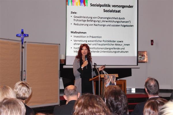 Frau mit Mikrofon vor einer Projektion zum Thema Ziele und Maßnahmen staatlicher Sozialpolitik (Caritasverband Darmstadt e. V.)
