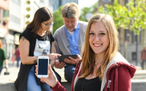 junge blonde Frau mit Smartphone in der Hand blickt in die Kamera