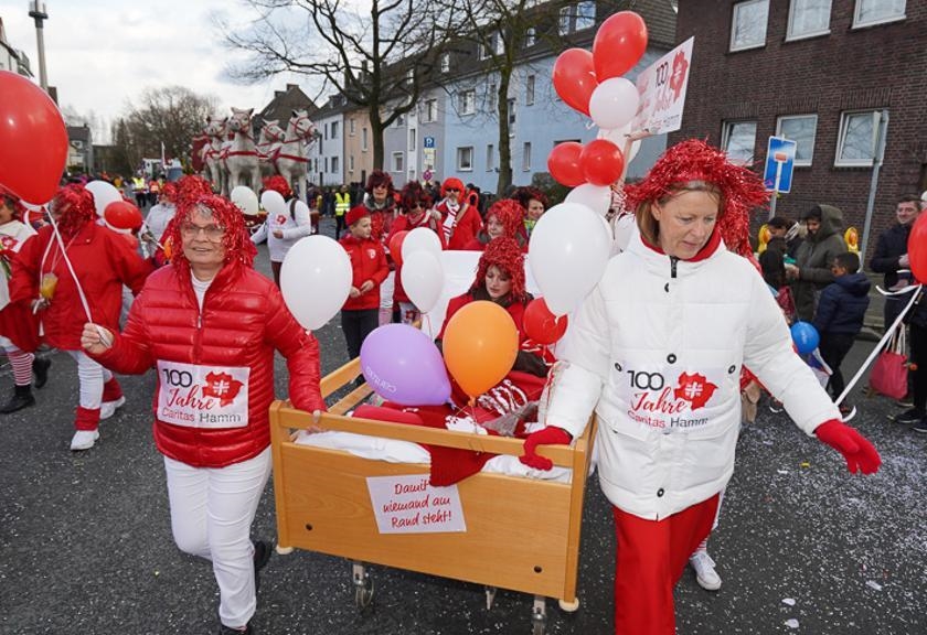 Rot-weiß gekleidete Frauen mit roten Perücken schieben ein Pflegebett (WA Szkudlarek)