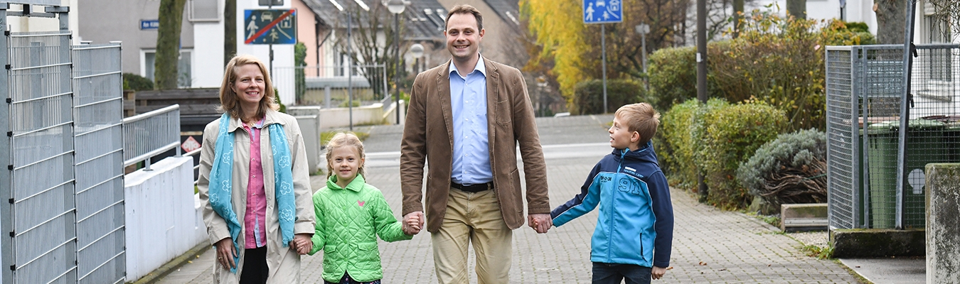 Mutter, Tochter, Vater und Sohn laufen gut gelaunt Hand in Hand die Straße entlang