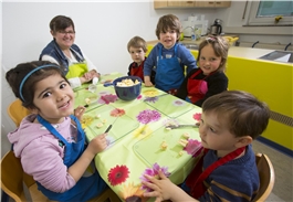 Mehrere Kinder sitzen an einem Küchentisch und schneiden Bananen in Stücke / Dietmar Wäsche
