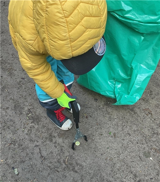 Ein Kind hebt mit einer Zange Müll vom Boden auf