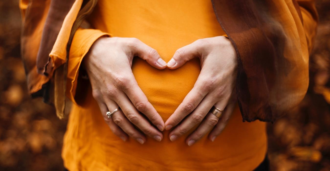 Schwangerschaftsbauch mit zum Herz geformten Händen