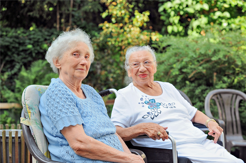Zwei Seniorinnen sitzen auf Gartenstühlen in einer Parkanlage