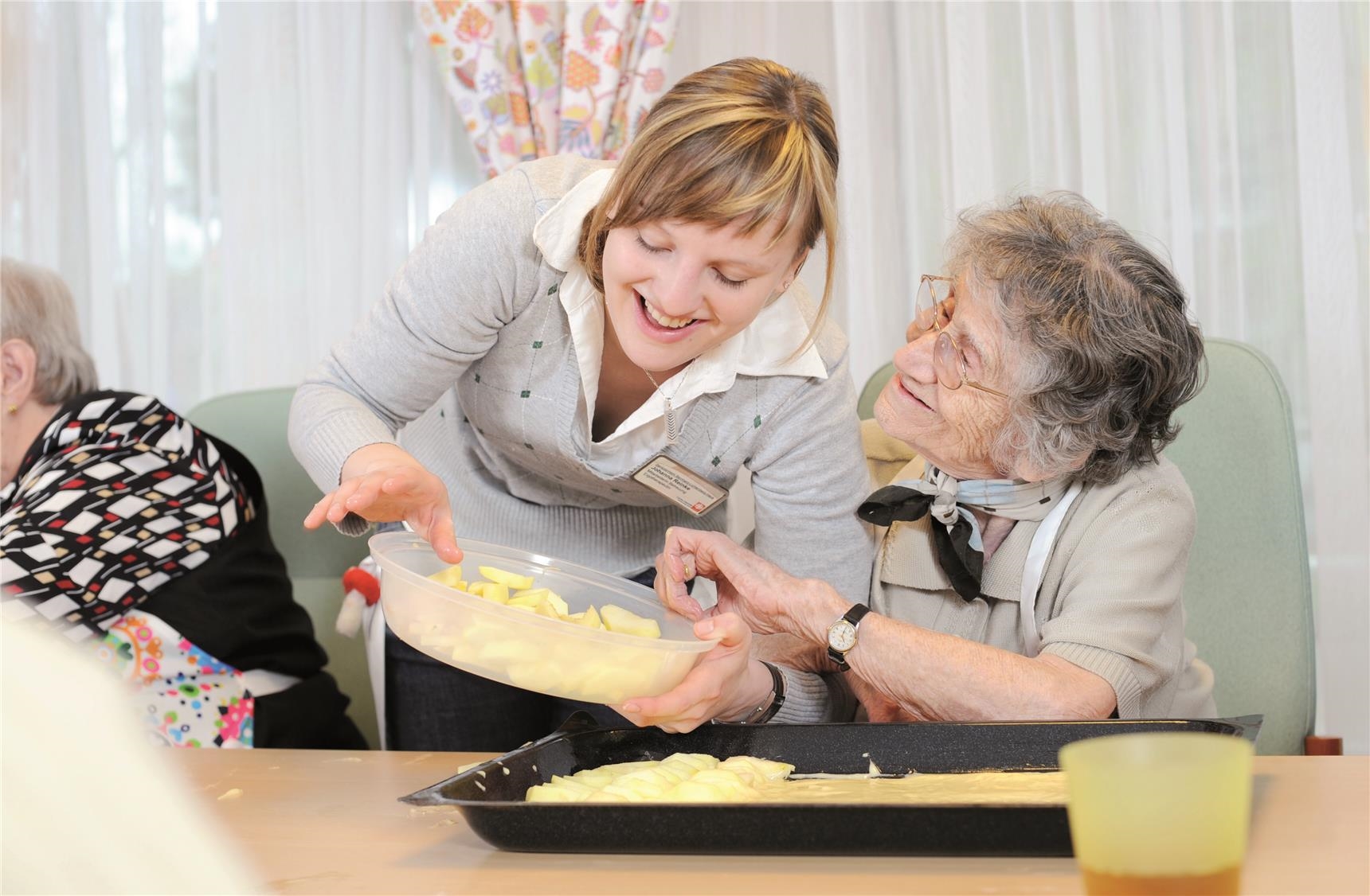 Betreuungsmitarbeiterin backt Kuchen mit Seniorin 