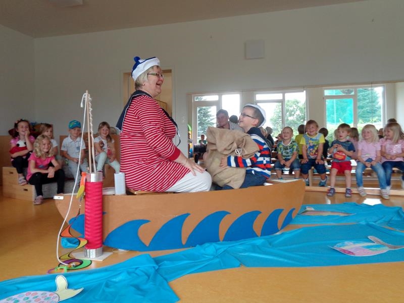 Frau sitzt mit Kind in einem Pappboot und spielt anderen Kindern ein Theaterstück vor 