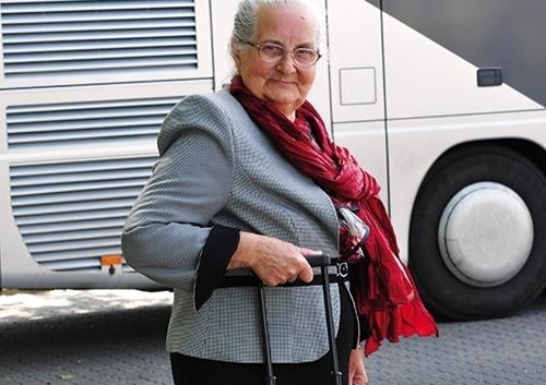 Seniorin steht mit Rollkoffer vor Reisebus