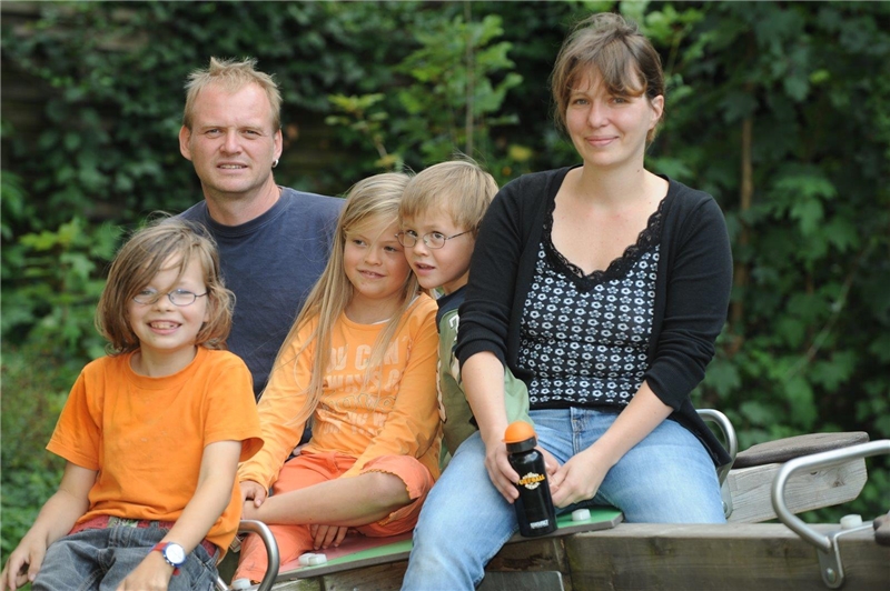 Mann, Frau und drei Kinder sitzen auf einer Wippe.