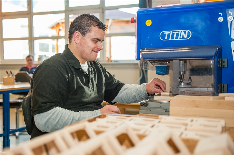 Mann sortiert Holzteile vor einer großen Maschine (©caritasverband bocholt)