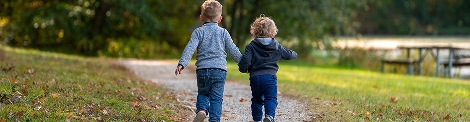 Zwei Kinder gehen auf einem Spazierweg und halten sich die Händer. 