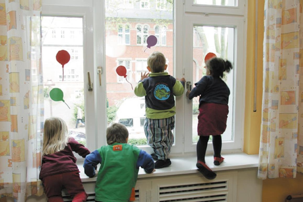 Kinder mit dem Rücken zum Betrachter stehen nebeneinander und schauen aus dem Fenster 