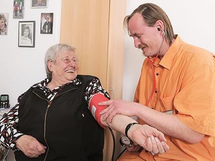 Altenpfleger misst Blutdruck bei Bewohnerin im Zimmer des Seniorenheimes 