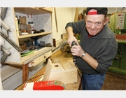 Das Bild zeigt einen Mitarbeiter der Schreinerei, der gerade einen Nistkasten zusammenschraubt. In dem Regal neben seinem Arbeitsplatz sind die Schreinerwerkzeuge, die er zu seiner Arbeit braucht, aufbewahrt.