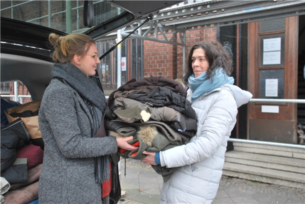 Eine junge Mitarbeiterin vom Pluspunkt überreicht einen Stapel Winterjacken an eine Mitarbeiterin von bodo