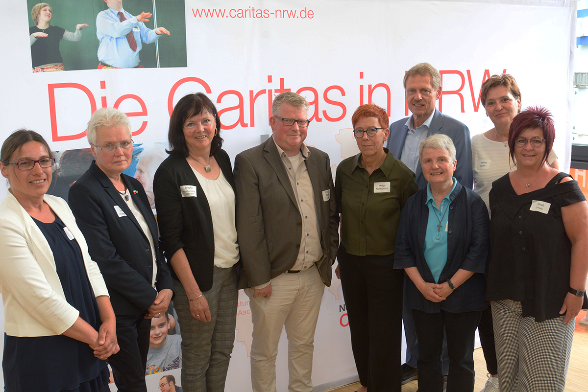 Gruppenfoto mit den Akteurinnen und Akteuren der CiNW-Fachtagung zur Umsetzung des Pflegeberufegesetzes in Essen vor einem Faltdisplay der Caritas in NRW (Foto: Caritas | Christoph Grätz)