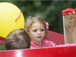 Ein Mädchen sitzt draußen auf einem Spielgerät. Sie hält einen Luftballon in der Hand. / Dietmar Wäsche