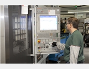 Dieses Bild zeigt einen Mitarbeiter der am Bedienpult einer CNC-gesteuerten Drehmaschine Einstellungen vornimmt.