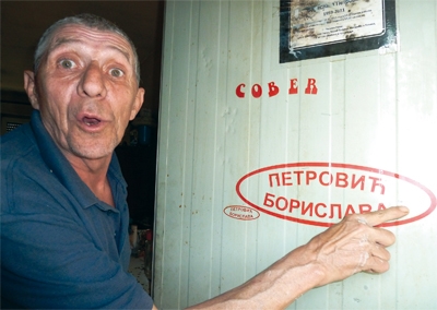 Ein Mann names „Ein-Zahn“ steht vor einem weißen Container und deutet auf eine Aufschrift (Alexander Richter)