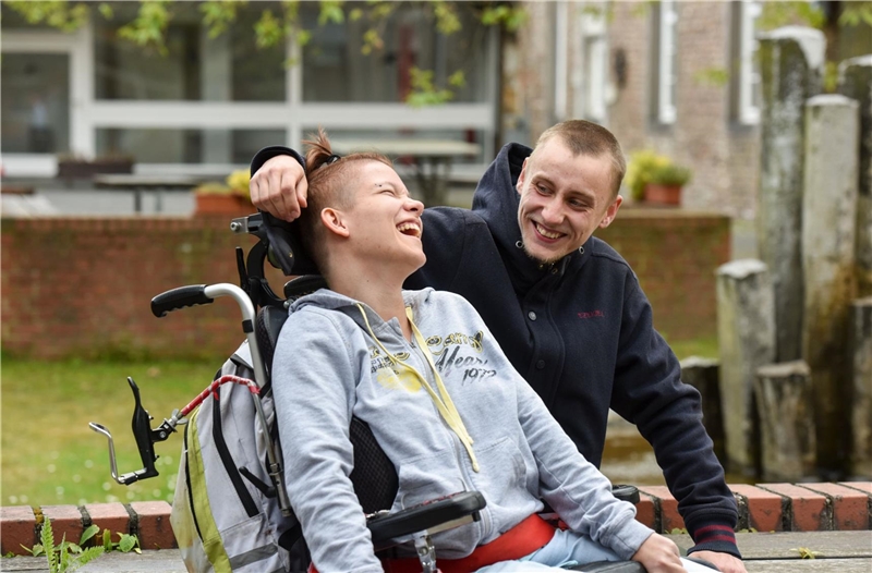 Lachende junge Frau im Rollstuhl mit Betreuer