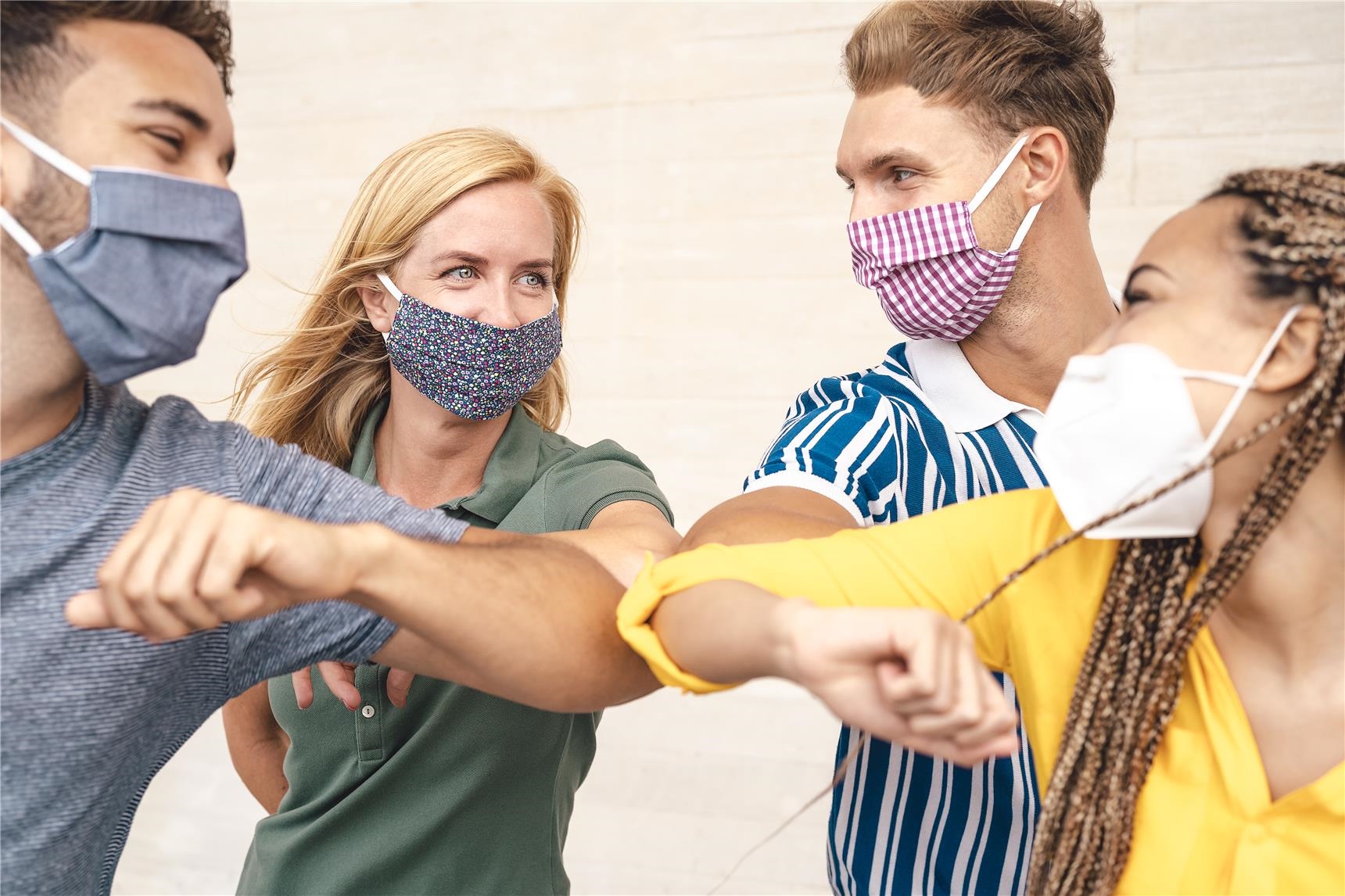 Junge Freunde tragen Gesichtsmaske und begrüßen sich mit dem Ellenbgen