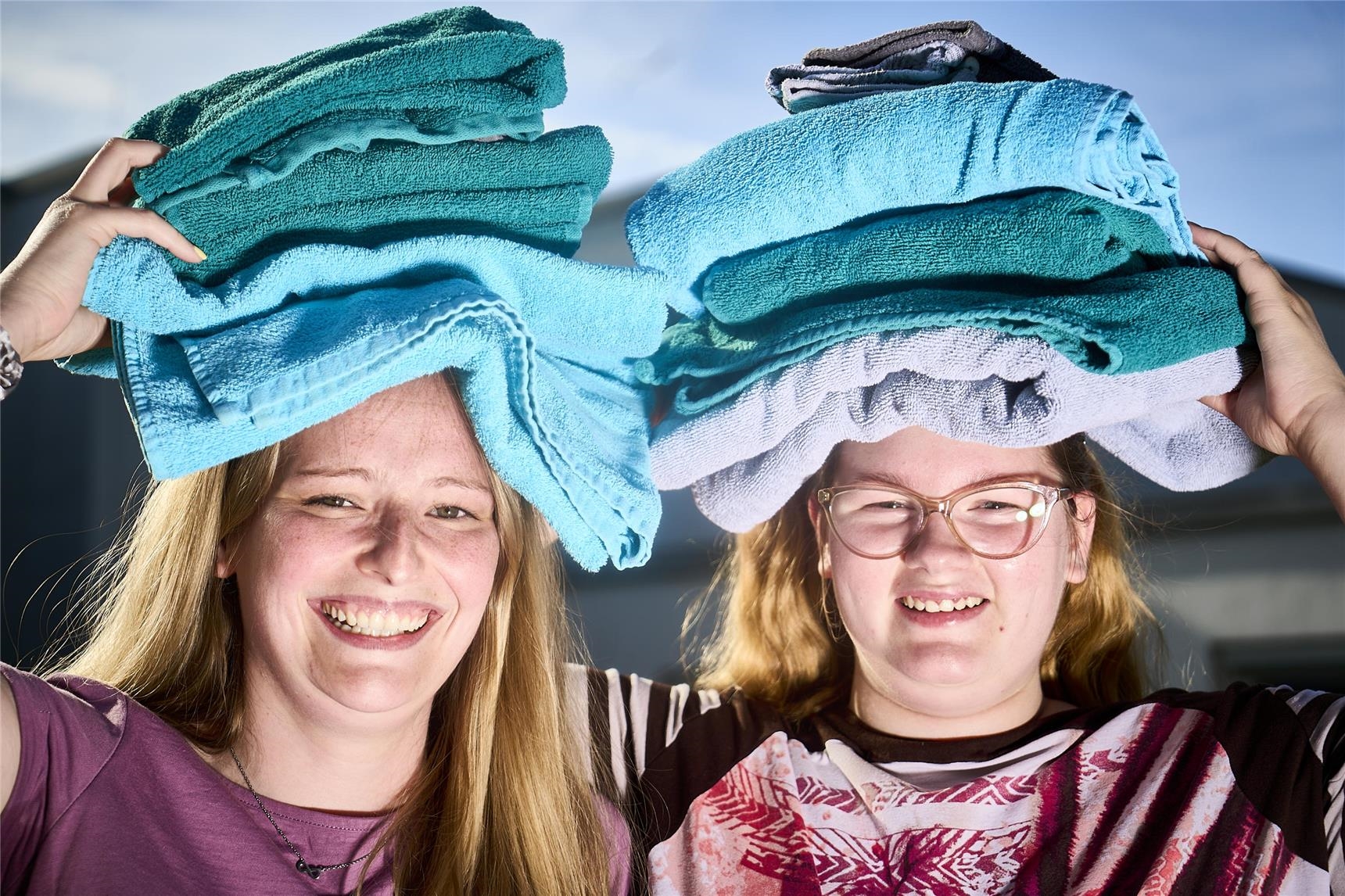 Eine Betreuerin und eine Klientin halten einen Stapel frischer Handtücher über den Kopf. 