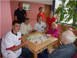 Mehrere junge Leute sitzen mit Senioren um einen Tisch und spielen Mensch ärgere dich nicht / Foto: Schedlbauer