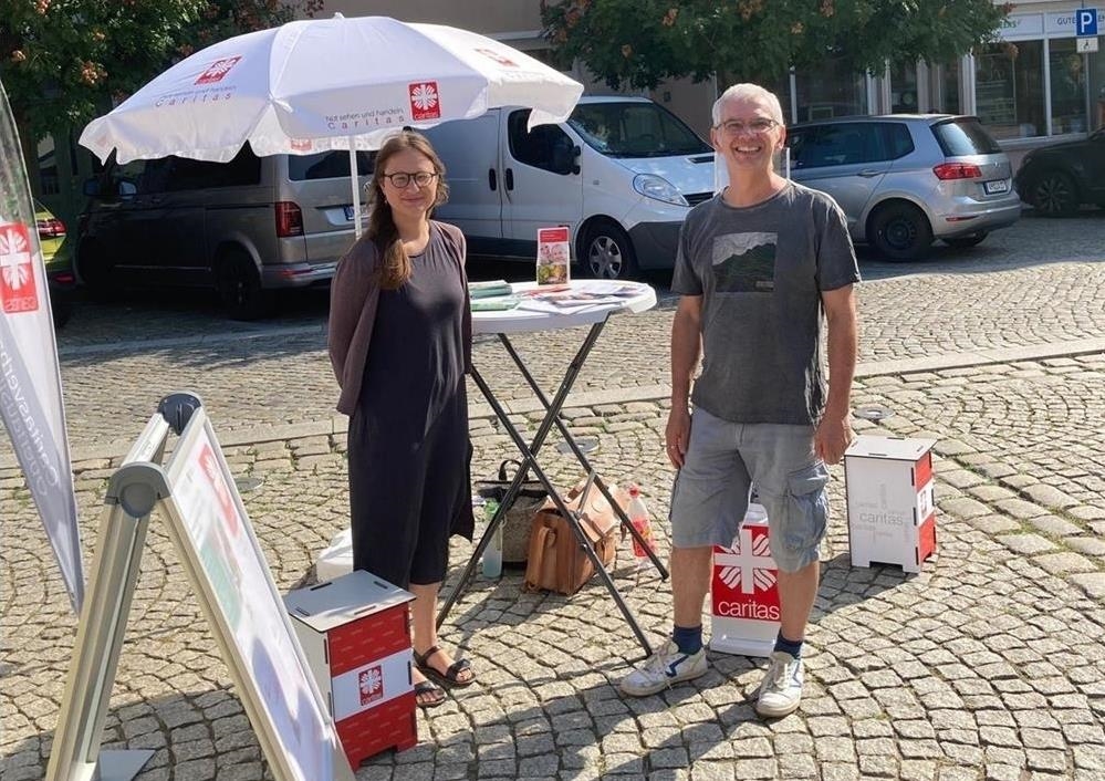 eine Frau und ein Mann vor einem kleinen Stand auf einem Marktplatz