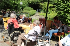 eine Gruppe von Bewohnern, zum Teil im Rollstuhl, sitzt zusammen am Tisch im Garten / Caritashaus Simeon