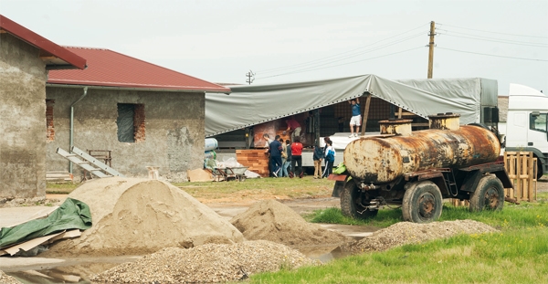 Ein Hof auf der Farm des Vereins IMPREUNA. Im Hintergrund laden Menschen neben dem Farmhaus Fracht von einem LKW ab. Im Vordergrund steht ein verosteter Tankanhänger und ein Sandhaufen. (Gerd Vieler)