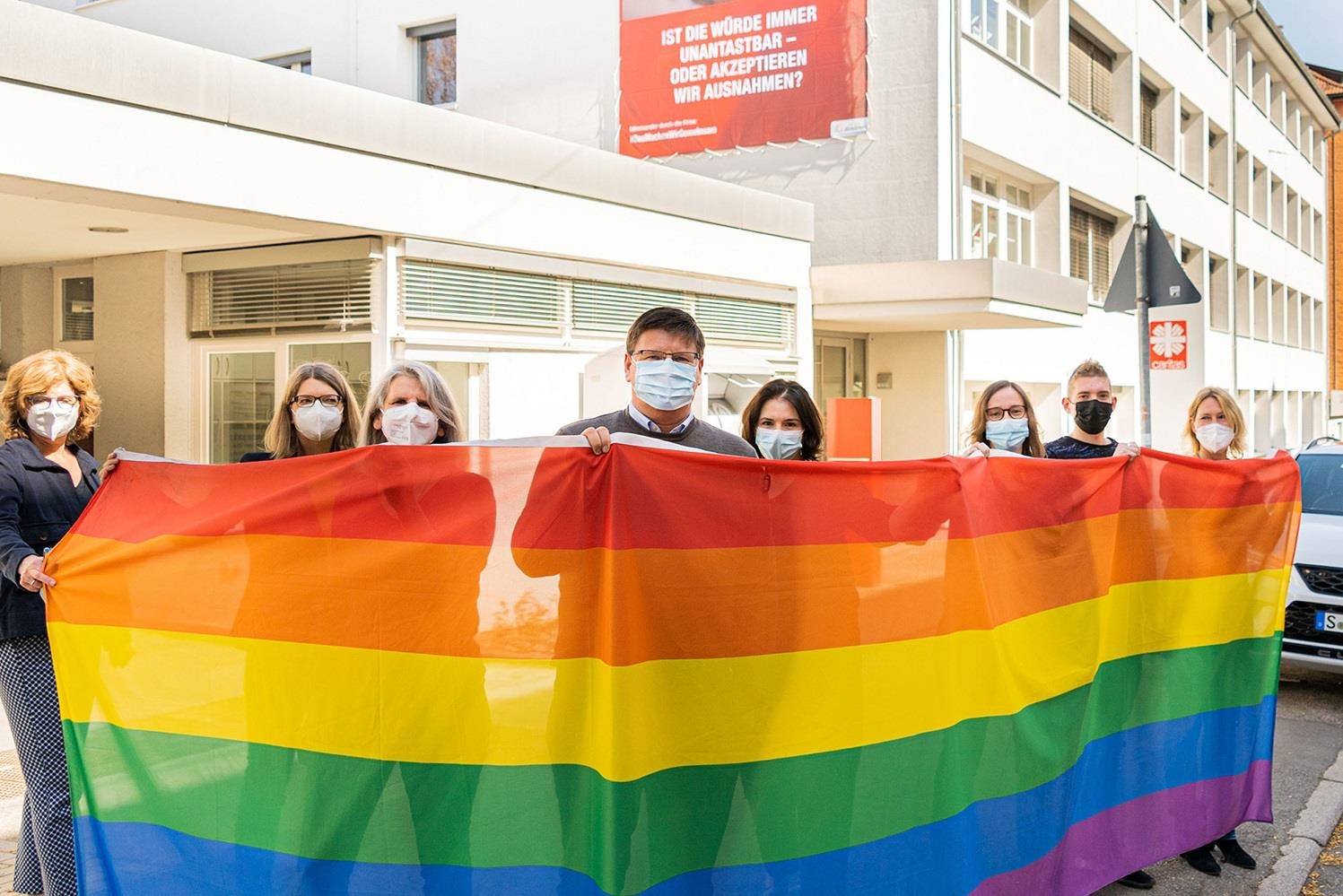 Caritas-Mitarbeitende halten eine Regenbogenfahne vor dem Haus der Caritas in Stuttgart-Ost.